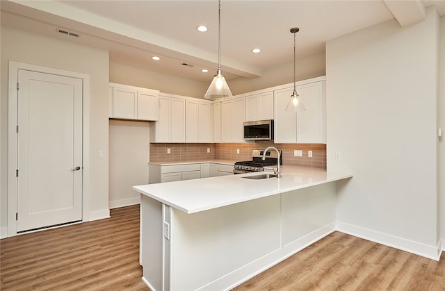 kitchen with stainless steel appliances, hanging light fixtures, white cabinets, and light hardwood / wood-style flooring