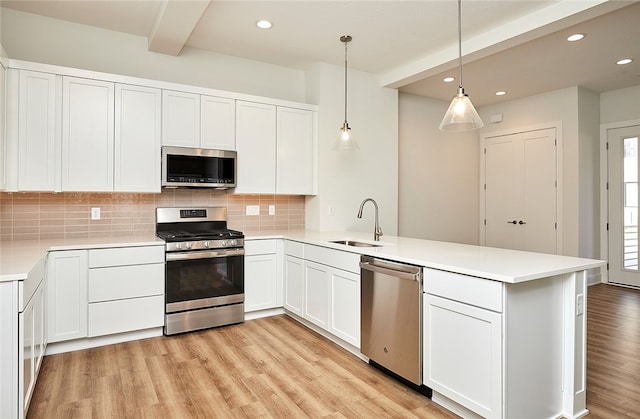 kitchen featuring pendant lighting, sink, kitchen peninsula, white cabinets, and appliances with stainless steel finishes