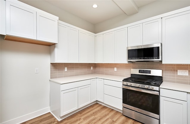 kitchen with appliances with stainless steel finishes, white cabinetry, backsplash, and light hardwood / wood-style flooring