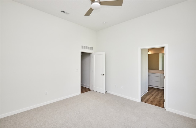 unfurnished bedroom with a high ceiling, ceiling fan, connected bathroom, and carpet