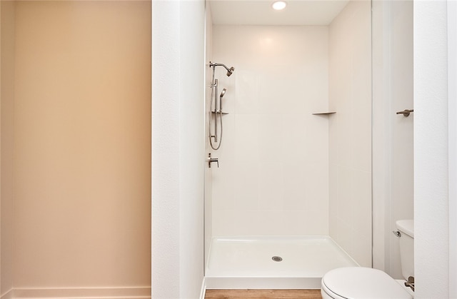 bathroom with a tile shower, toilet, and wood-type flooring