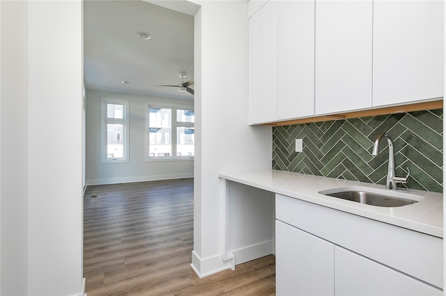 kitchen featuring ceiling fan, sink, backsplash, white cabinetry, and hardwood / wood-style floors