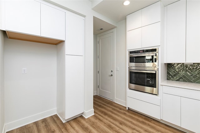 kitchen with double oven, decorative backsplash, white cabinetry, and light hardwood / wood-style floors