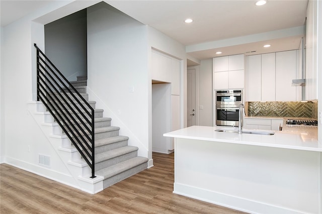 kitchen featuring light wood-type flooring, sink, stainless steel appliances, kitchen peninsula, and white cabinets