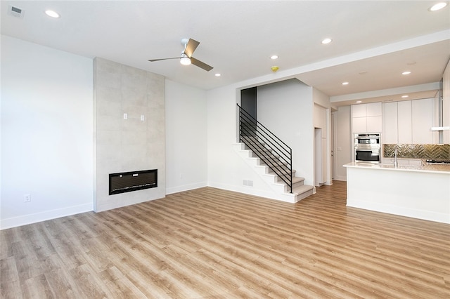 unfurnished living room featuring light wood-type flooring, a fireplace, and ceiling fan