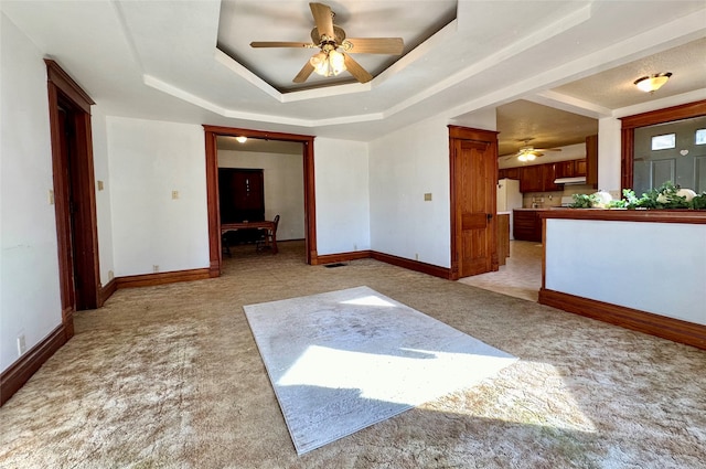 carpeted spare room with a raised ceiling and ceiling fan