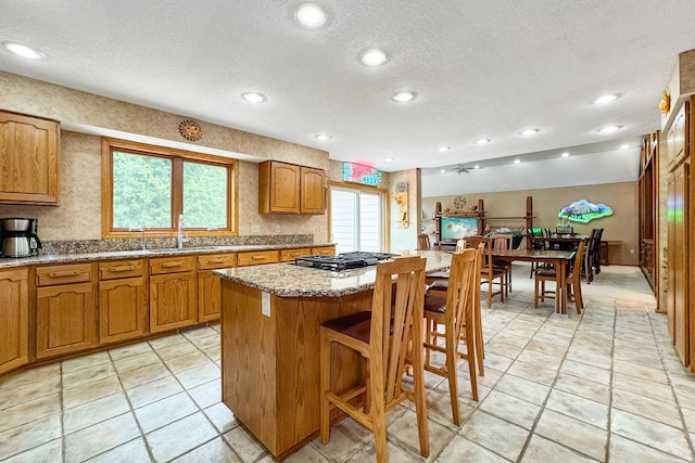 kitchen featuring stainless steel gas cooktop, light stone countertops, a kitchen bar, a center island, and a textured ceiling