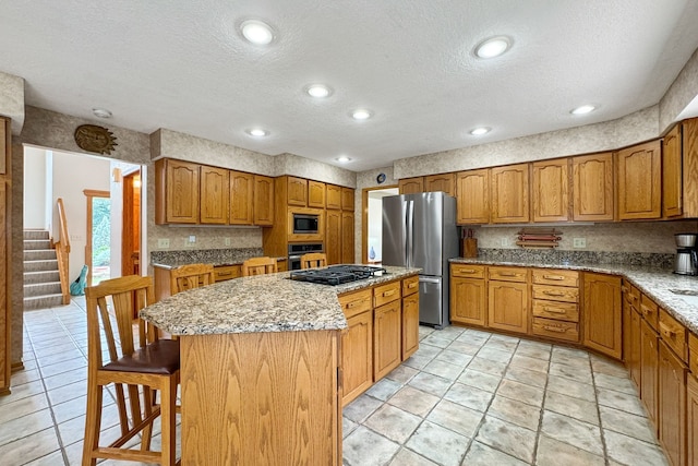 kitchen with stainless steel appliances, a kitchen island, light stone counters, and a textured ceiling