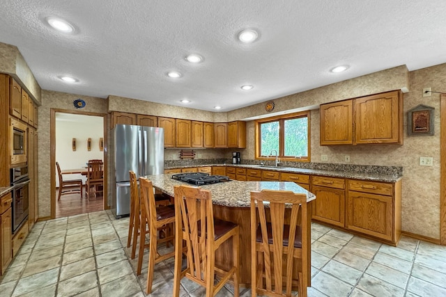 kitchen with a kitchen island, sink, light stone countertops, appliances with stainless steel finishes, and a textured ceiling