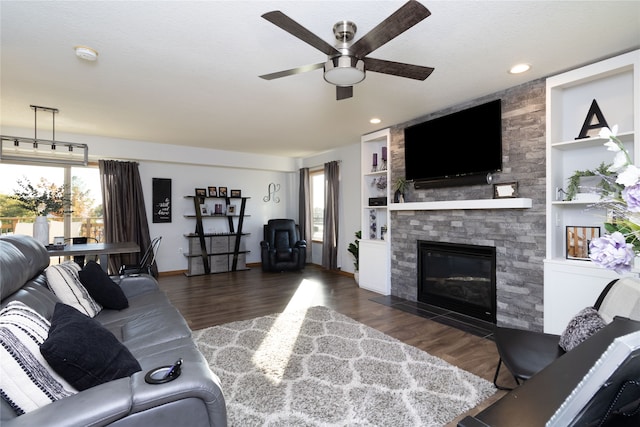 living room with dark wood-type flooring, built in features, a wealth of natural light, and a stone fireplace