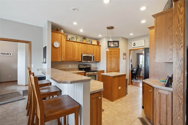 kitchen with pendant lighting, kitchen peninsula, stainless steel appliances, a center island, and a breakfast bar area