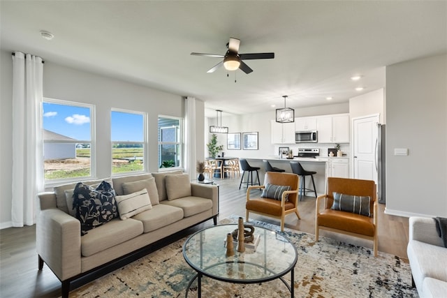 living room featuring ceiling fan with notable chandelier and light hardwood / wood-style flooring