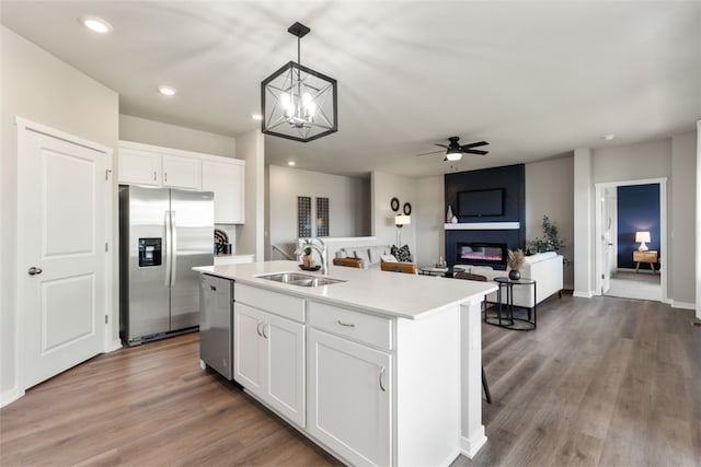 kitchen with stainless steel appliances, sink, decorative light fixtures, a center island with sink, and white cabinets