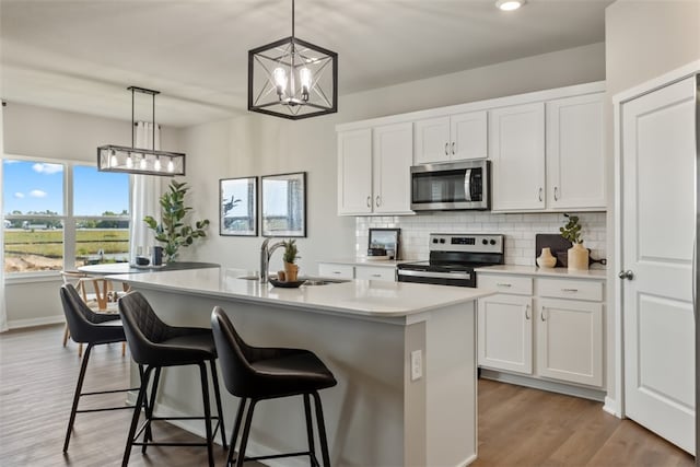 kitchen featuring white cabinets, hanging light fixtures, an island with sink, and stainless steel appliances