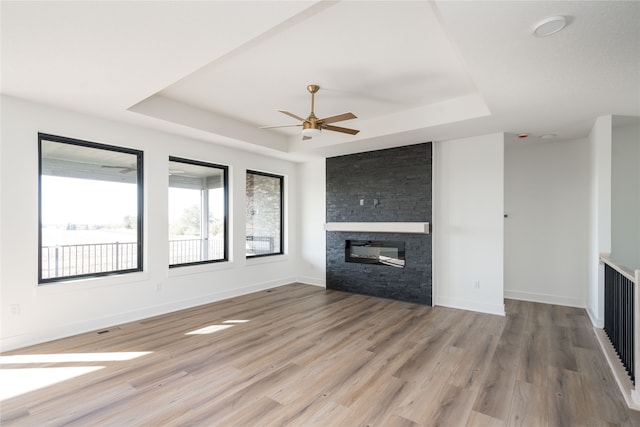 unfurnished living room featuring a fireplace, ceiling fan, wood-type flooring, and a raised ceiling