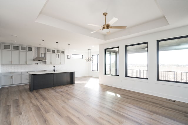 kitchen featuring wall chimney range hood, a kitchen island with sink, hardwood / wood-style floors, and a raised ceiling