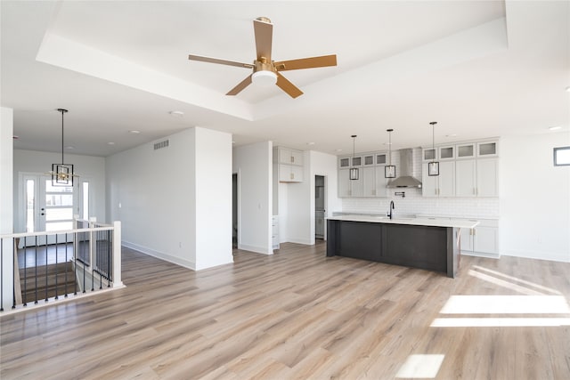 kitchen with pendant lighting, white cabinets, a center island with sink, and a tray ceiling