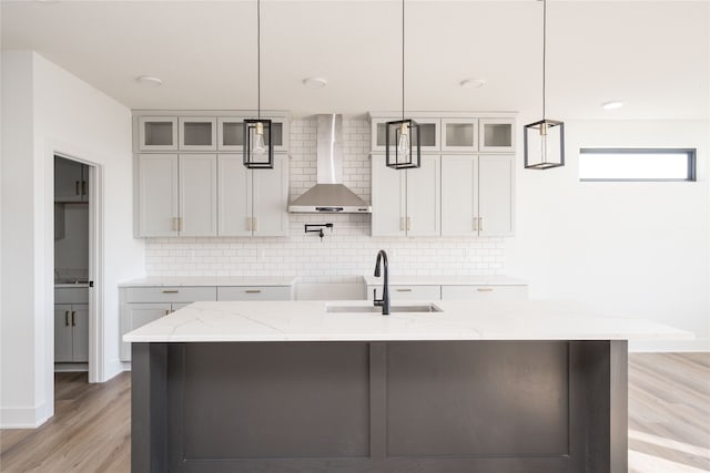 kitchen with pendant lighting, light stone counters, wall chimney range hood, and sink