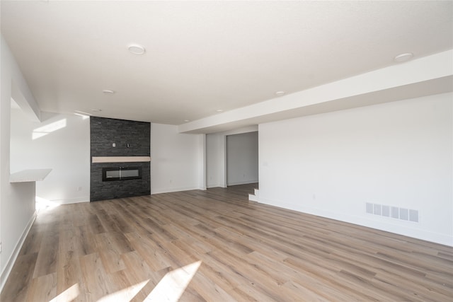 unfurnished living room featuring a stone fireplace and light hardwood / wood-style floors