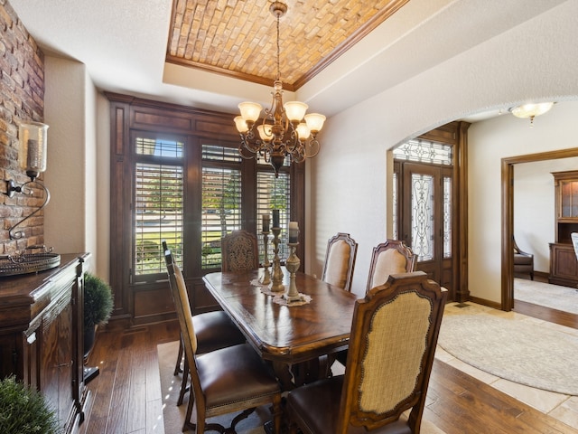 dining room featuring a raised ceiling, a chandelier, dark wood-type flooring, and crown molding