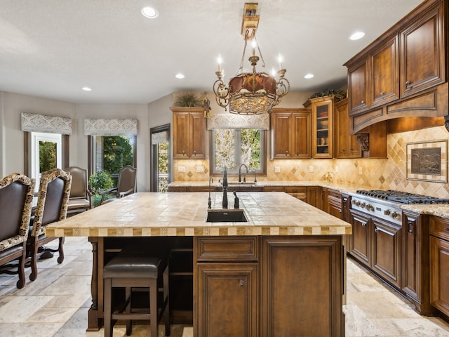 kitchen with stainless steel gas stovetop, an inviting chandelier, a center island with sink, and sink