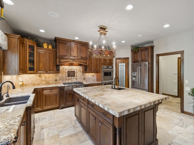 kitchen with appliances with stainless steel finishes, a kitchen island with sink, sink, and a chandelier