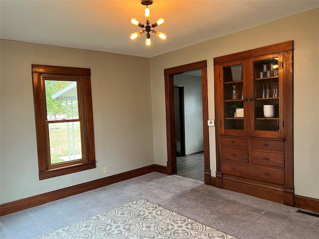 carpeted spare room featuring a textured ceiling and a chandelier