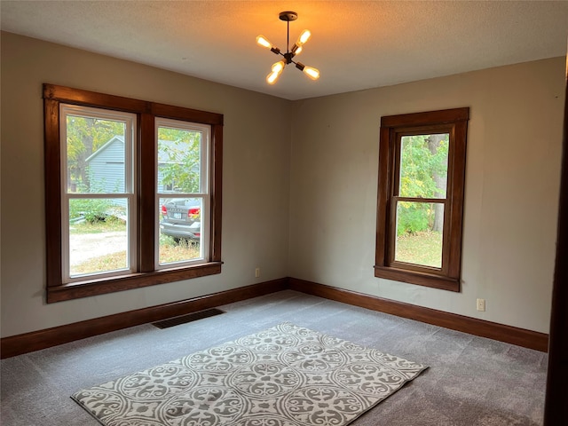 carpeted empty room featuring a notable chandelier, plenty of natural light, and a textured ceiling