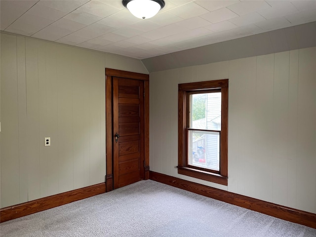 unfurnished room with lofted ceiling, wood walls, and carpet