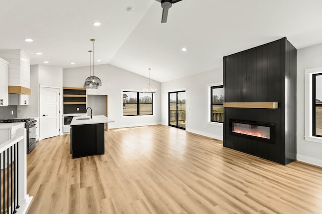 kitchen with white cabinets, pendant lighting, a center island with sink, stainless steel gas range oven, and light hardwood / wood-style floors