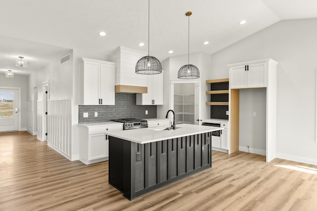 kitchen featuring an island with sink, pendant lighting, white cabinetry, and light hardwood / wood-style floors