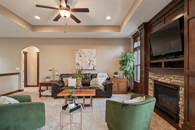 carpeted living room with ceiling fan, a fireplace, and a raised ceiling