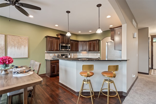 kitchen featuring dark stone counters, dark hardwood / wood-style floors, decorative light fixtures, stainless steel appliances, and backsplash