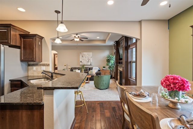 kitchen with ceiling fan, sink, decorative light fixtures, dark stone counters, and dark hardwood / wood-style flooring