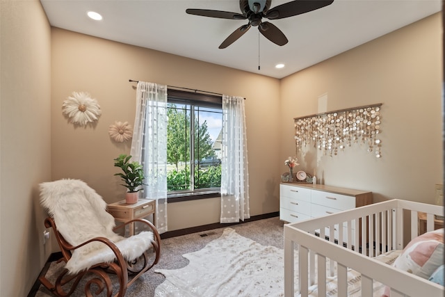 bedroom with ceiling fan, a nursery area, and carpet