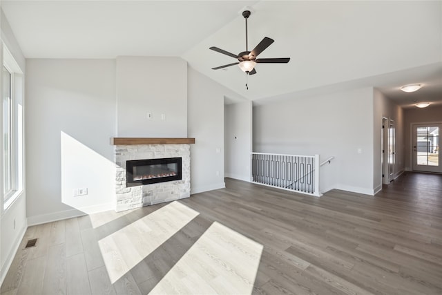 unfurnished living room with ceiling fan, a stone fireplace, and dark hardwood / wood-style flooring