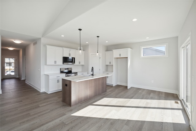 kitchen featuring a kitchen island with sink, white cabinets, decorative light fixtures, appliances with stainless steel finishes, and light hardwood / wood-style floors