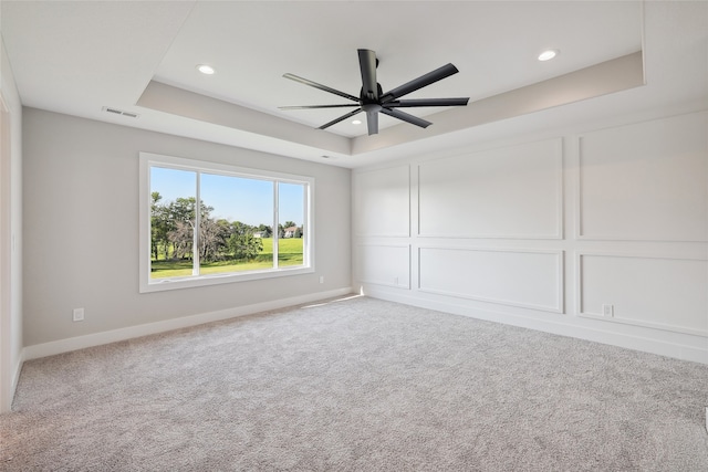 spare room with carpet, a tray ceiling, and ceiling fan