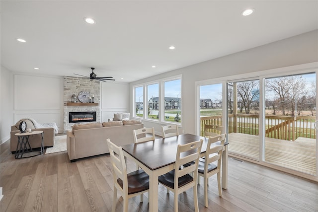 dining area with a fireplace, ceiling fan, and light hardwood / wood-style flooring