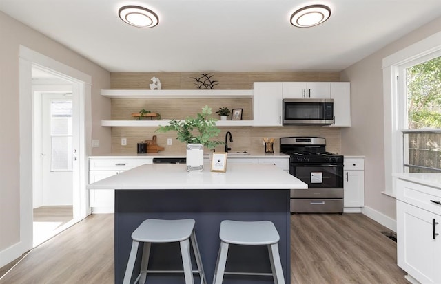 kitchen with backsplash, stainless steel appliances, wood-type flooring, a center island, and white cabinetry