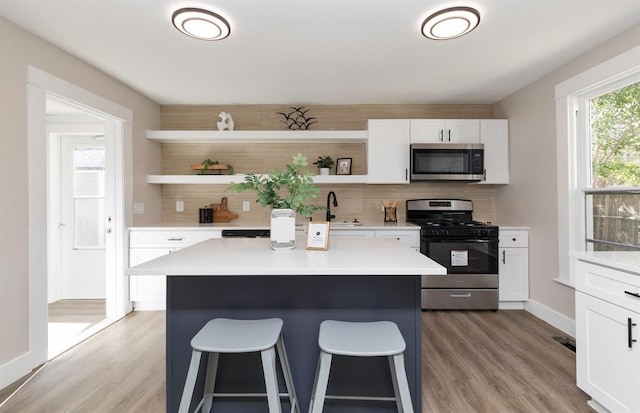 kitchen with white cabinets, decorative backsplash, a kitchen breakfast bar, stainless steel appliances, and open shelves