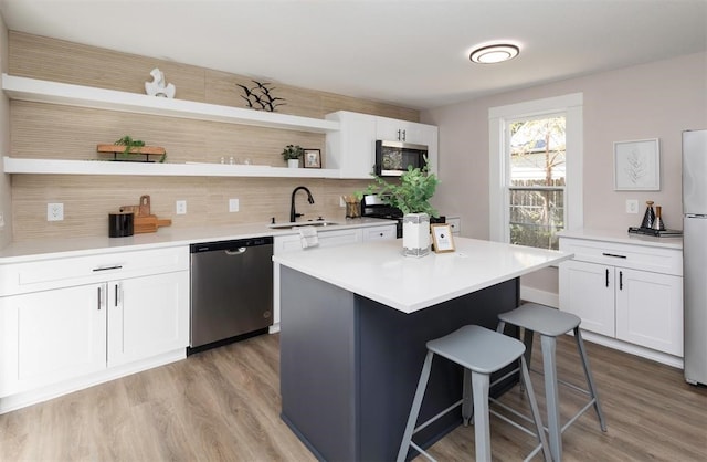 kitchen featuring appliances with stainless steel finishes, a breakfast bar, white cabinetry, open shelves, and a sink