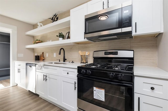 kitchen featuring open shelves, stainless steel appliances, tasteful backsplash, light countertops, and a sink