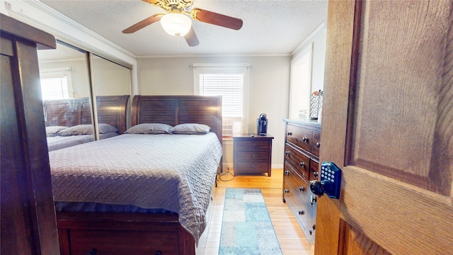 bedroom featuring a closet, ornamental molding, a textured ceiling, light hardwood / wood-style floors, and ceiling fan