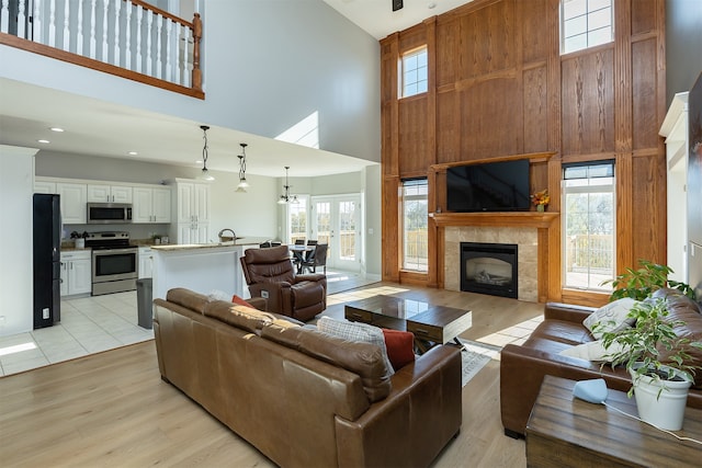 living area featuring plenty of natural light, light wood-type flooring, a high ceiling, and a tiled fireplace