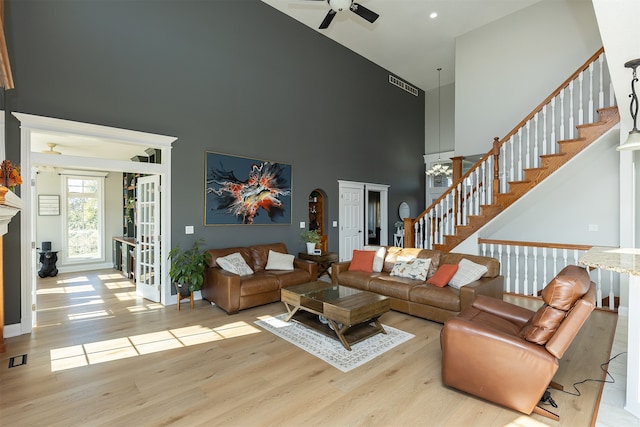 living area with baseboards, ceiling fan, stairs, a high ceiling, and light wood-type flooring