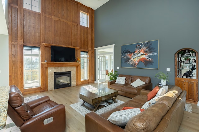 living area featuring light wood-type flooring, plenty of natural light, a fireplace, and a high ceiling