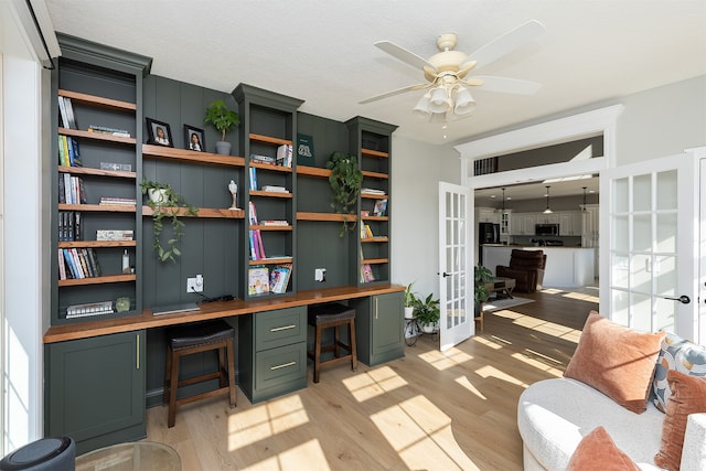 home office featuring light wood finished floors, ceiling fan, french doors, and built in study area