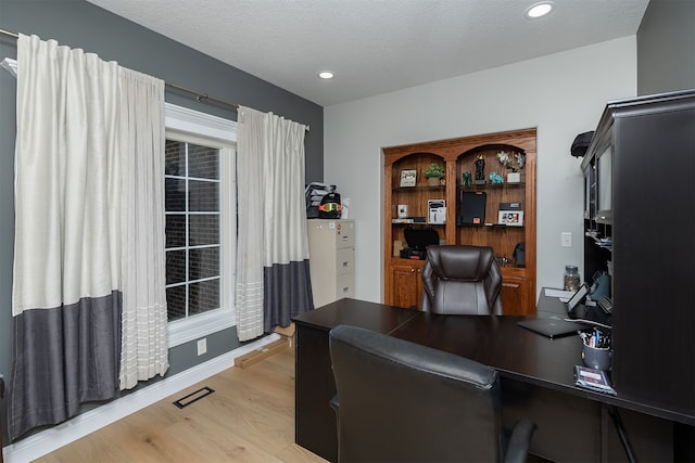 office space featuring light wood-type flooring, visible vents, a textured ceiling, and recessed lighting