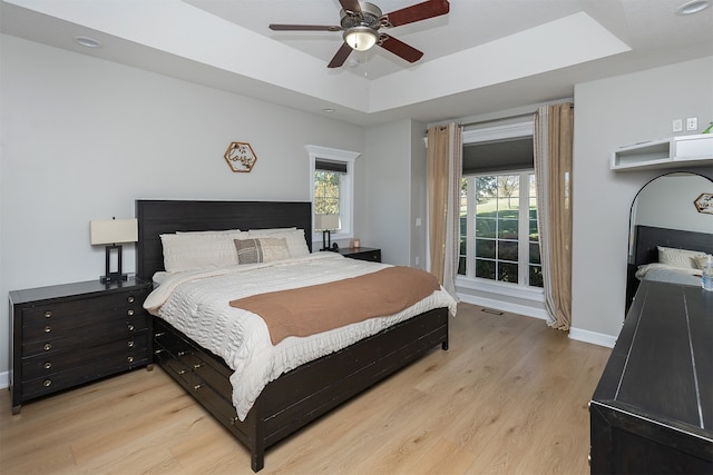 bedroom featuring baseboards, visible vents, ceiling fan, a tray ceiling, and light wood-type flooring